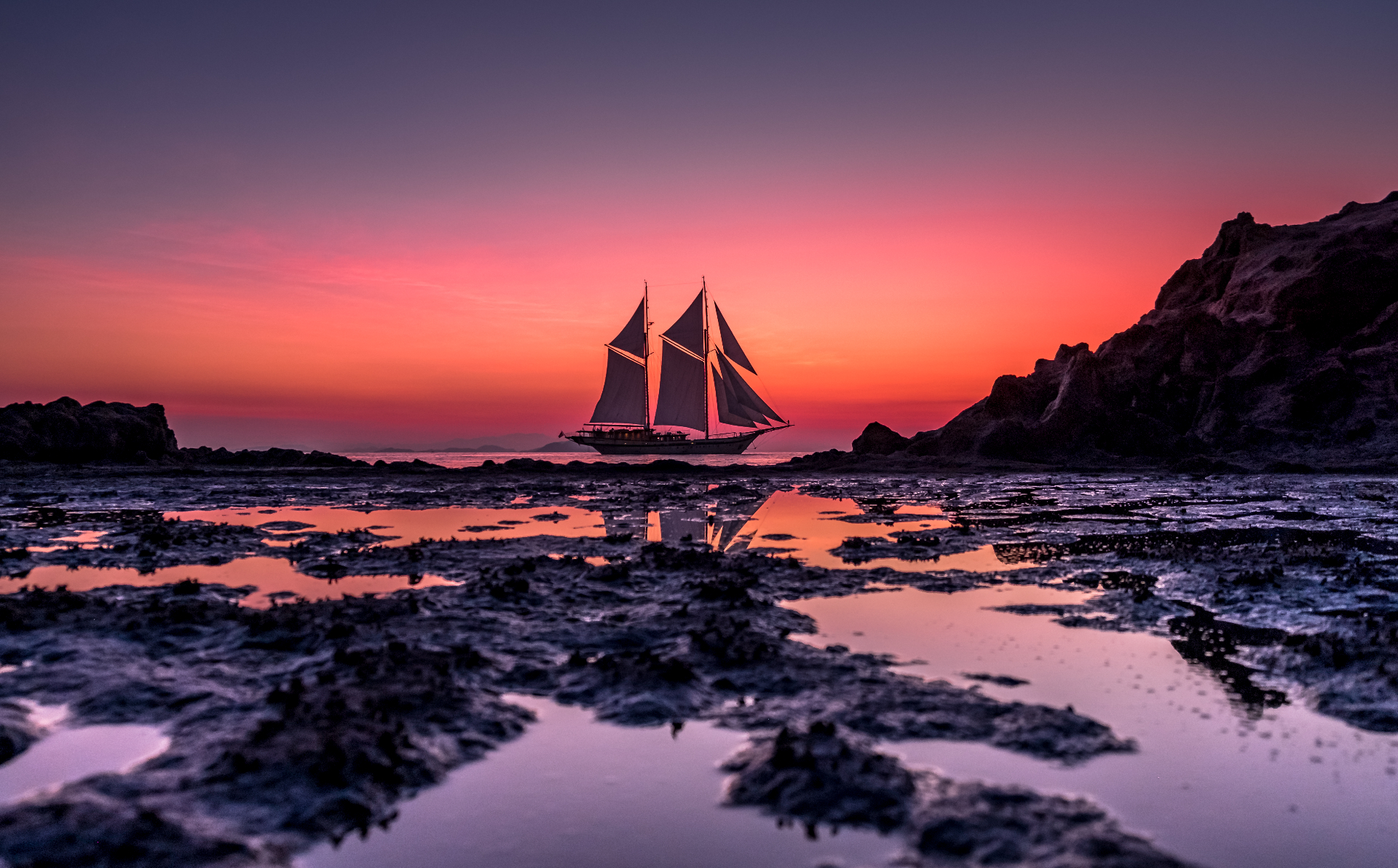 Lamima anchored at low tide with a pink and purple sunset reflected in rock pools