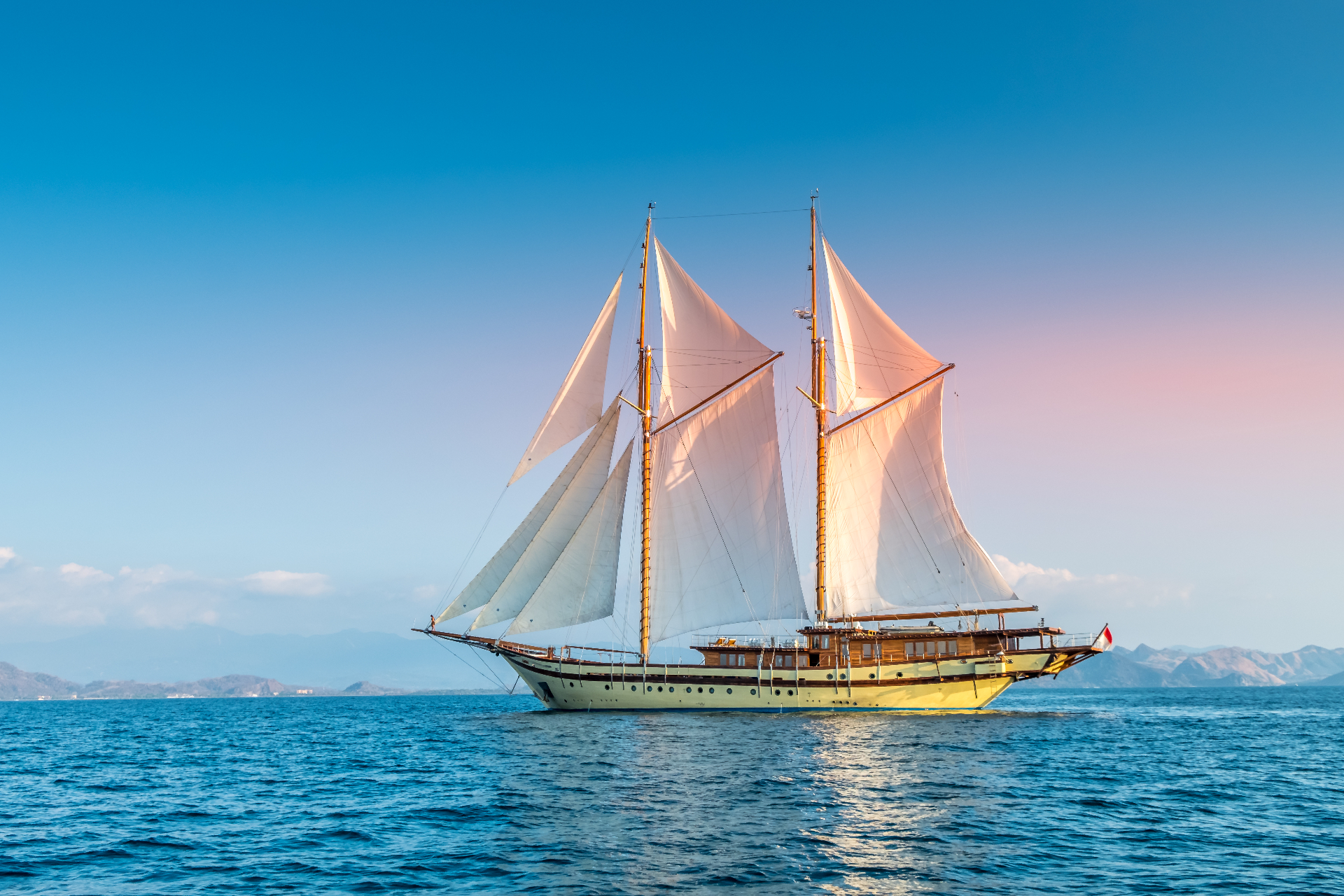 Lamima phinisi with white sails set against a clear blue sky off Flores
