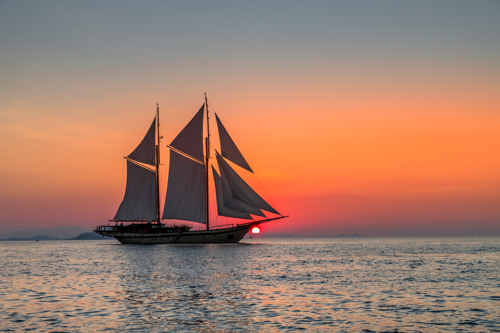 Lamima silhouetted against a burning orange sunset with the sun dipping behind the sails