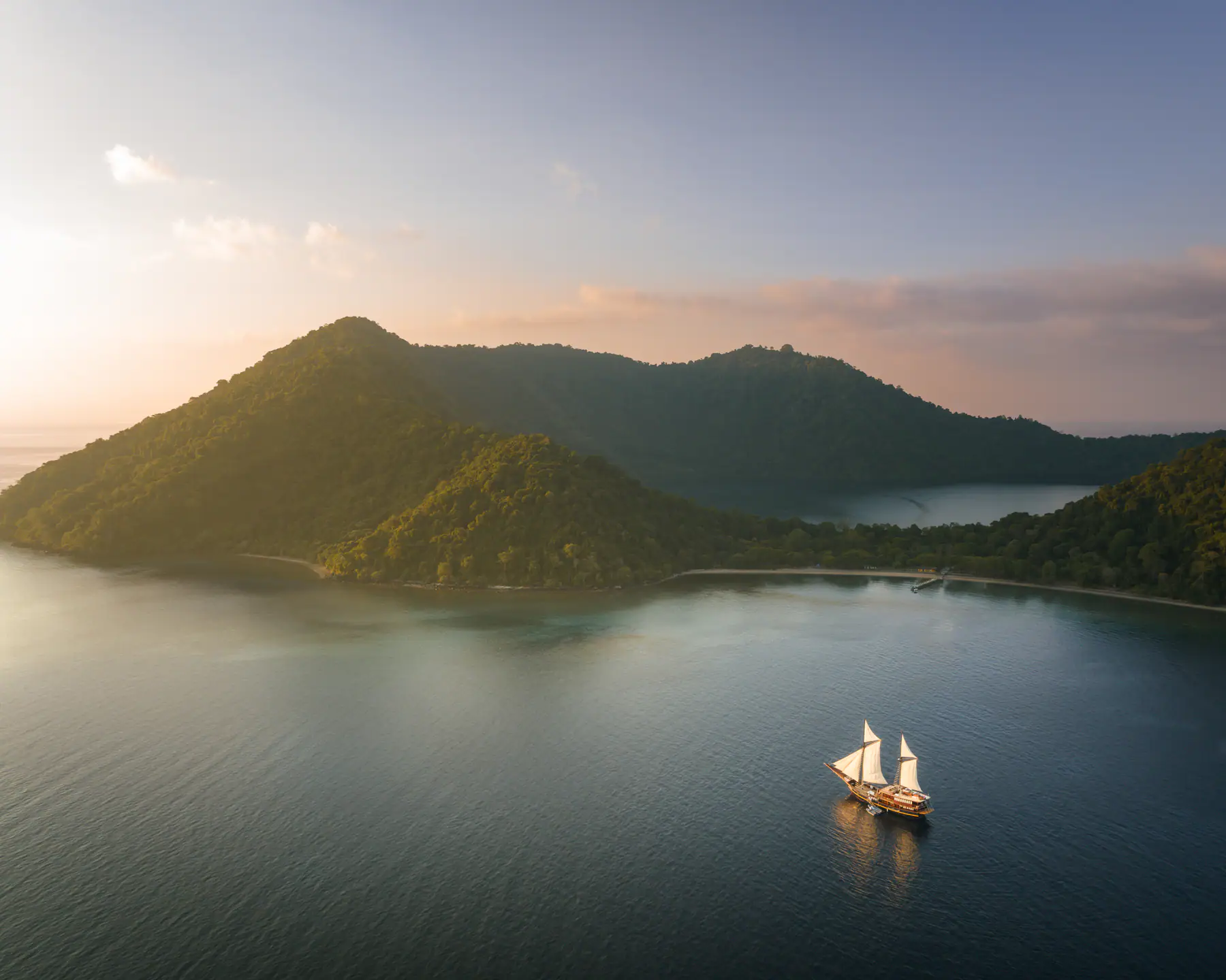 Celestia anchored at sunrise beside a jungle-covered island in Raja Ampat