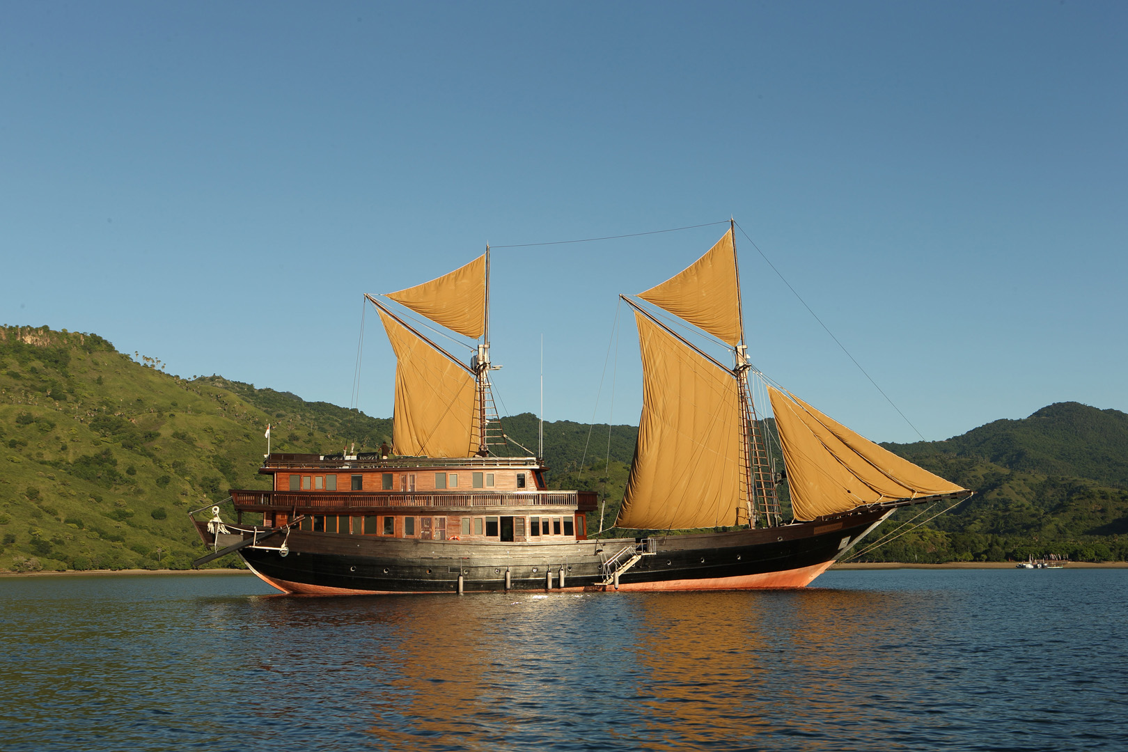 Broadside view of Alila Purnama phinisi with tan sails and hand-crafted teak superstructure