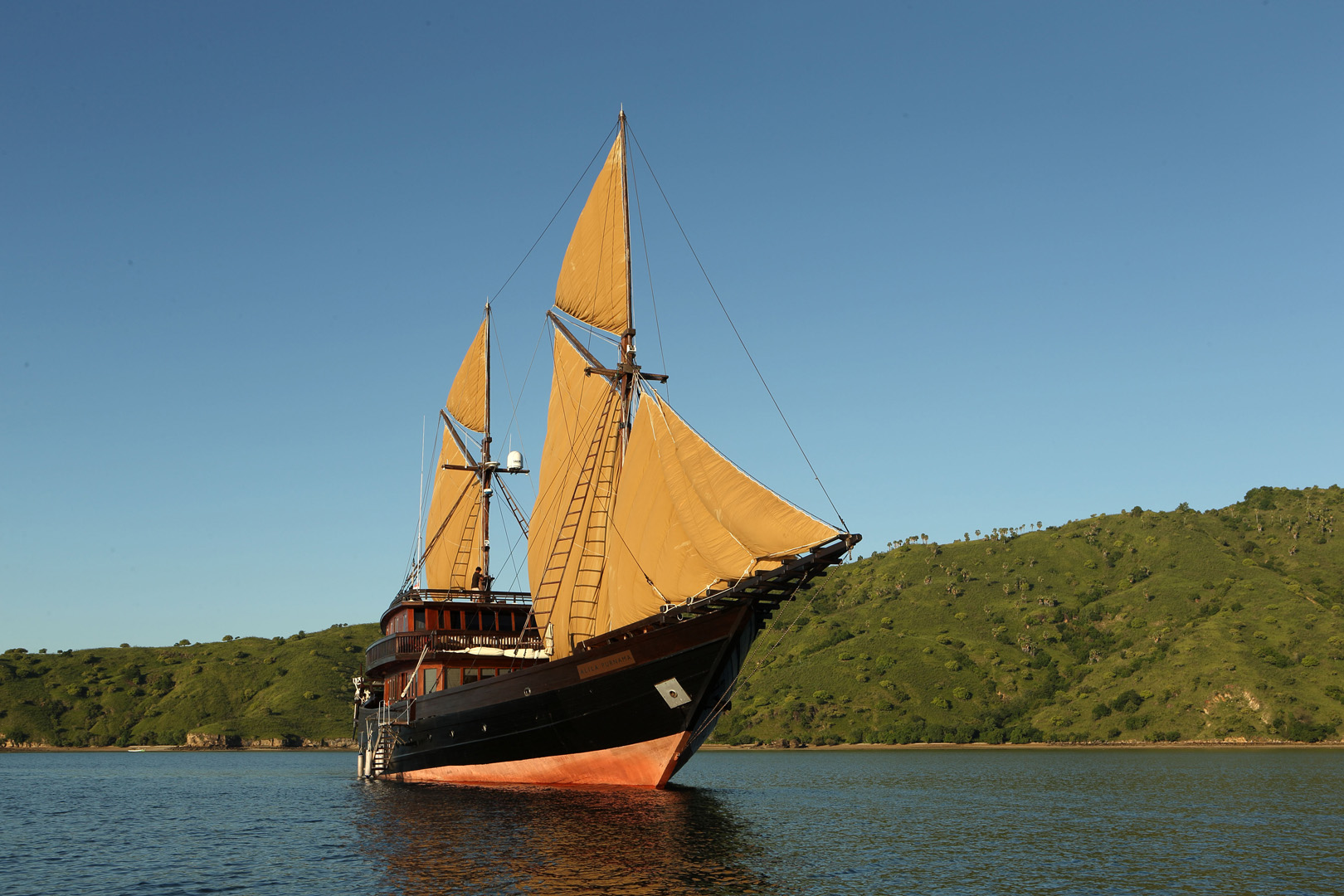 Alila Purnama traditional phinisi under full sail off a green Raja Ampat headland