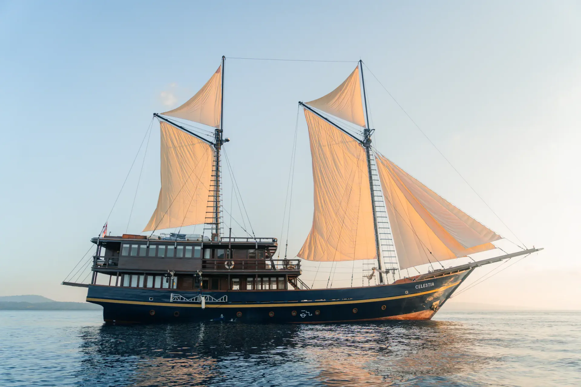 Celestia phinisi under full sail at golden hour — Raja Ampat private yacht charter