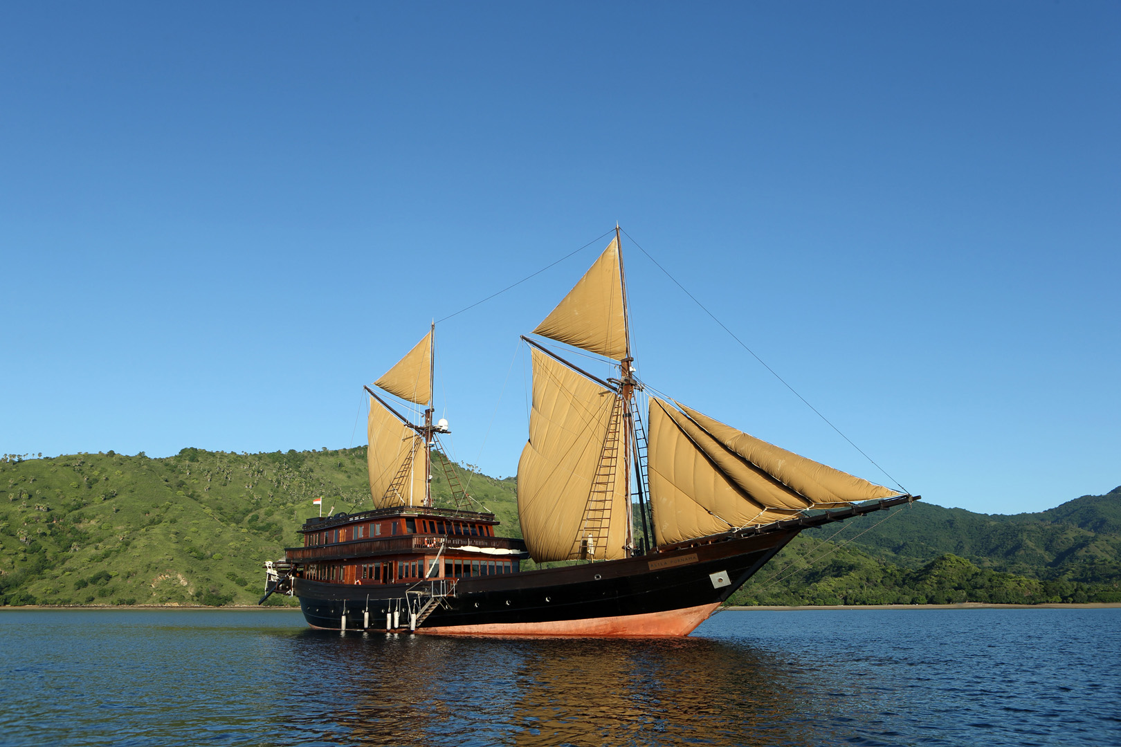 Alila Purnama sailing past a green Indonesian island with all sails set